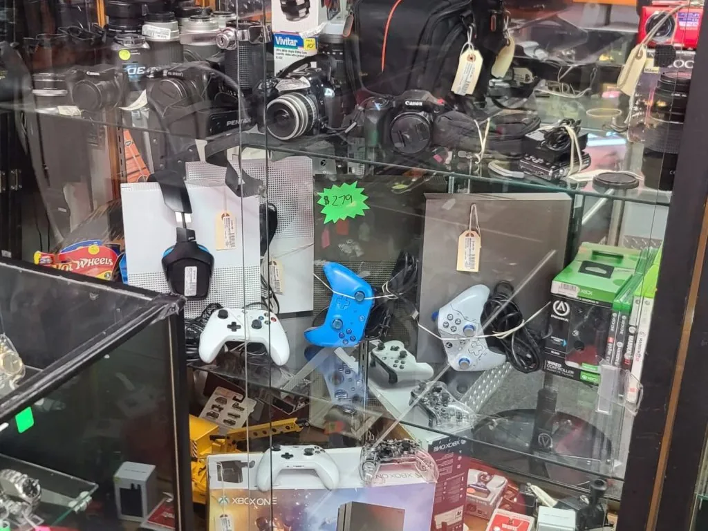 A locked display case of used cameras, Xbox consoles and controllers