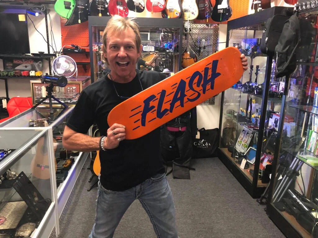 Rob Van Gronigen holding an orange ‘FLASH’ skateboard deck in The Fresno Hock Shoppe